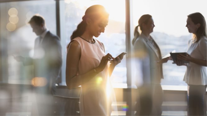 woman in foreground interacting with her mobile phone, with other people in the background